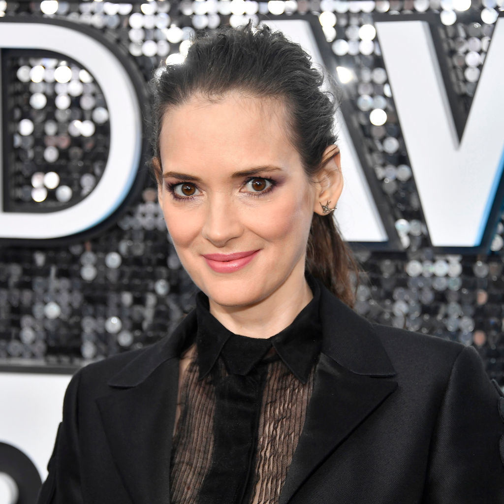 Winona Ryder in a semi-sheer blouse and black suit at an event