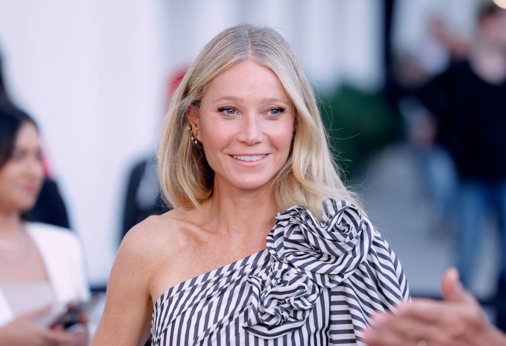 Gwyneth Paltrow smiling, wearing a striped outfit with a large bow on the shoulder