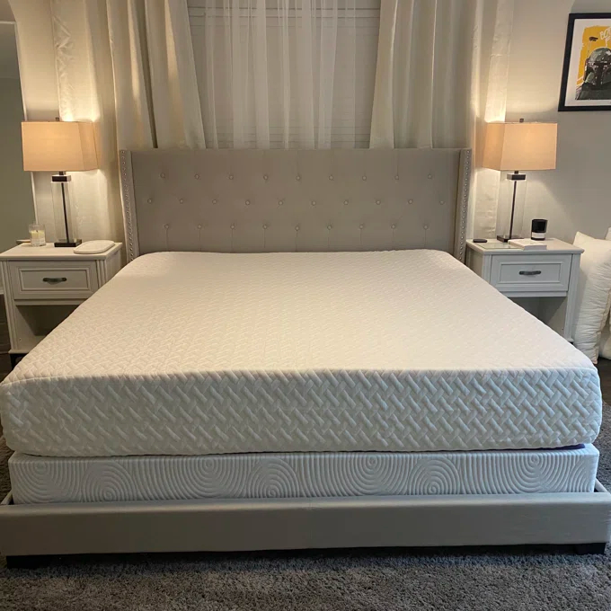 Reviewer&#x27;s photo of the mattress placed on an upholstered bedframe with a gray tufted headboard