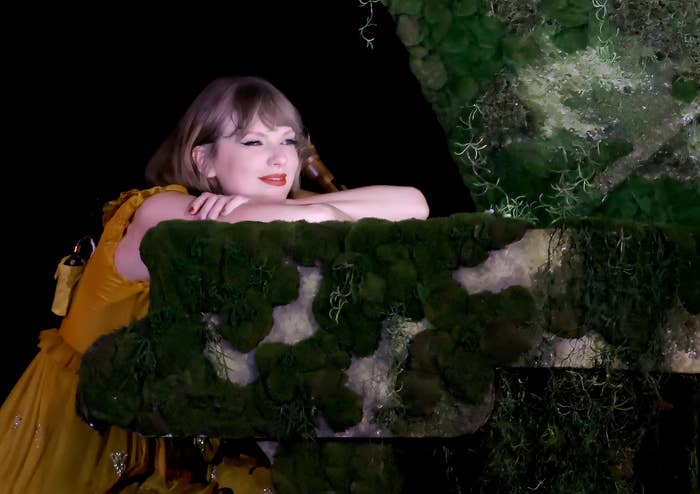 Taylor Swift leaning on a moss-covered balcony, wearing a yellow ruffled dress