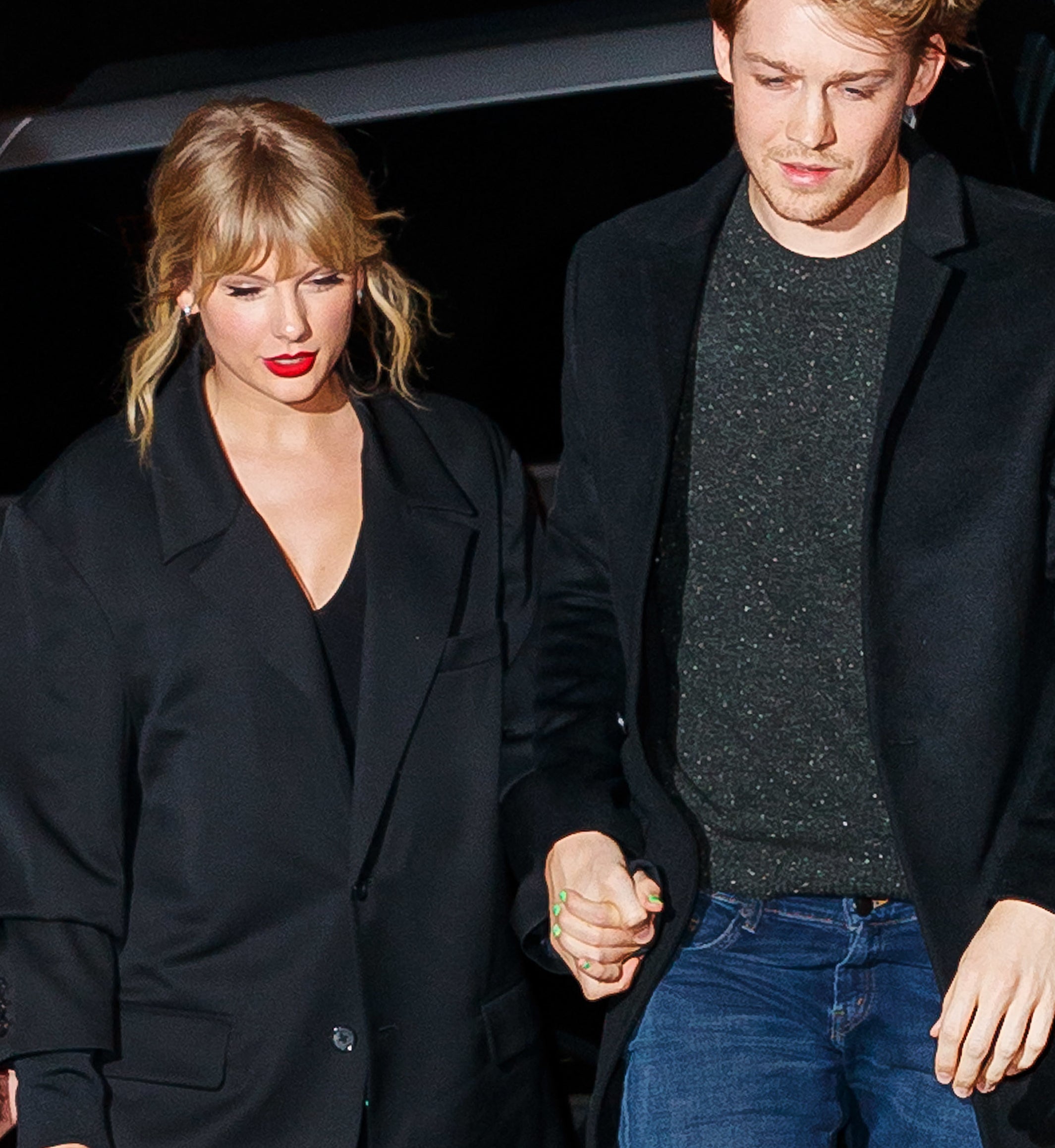 Taylor Swift in a sparkly outfit and Joe Alwyn in a black coat holding hands