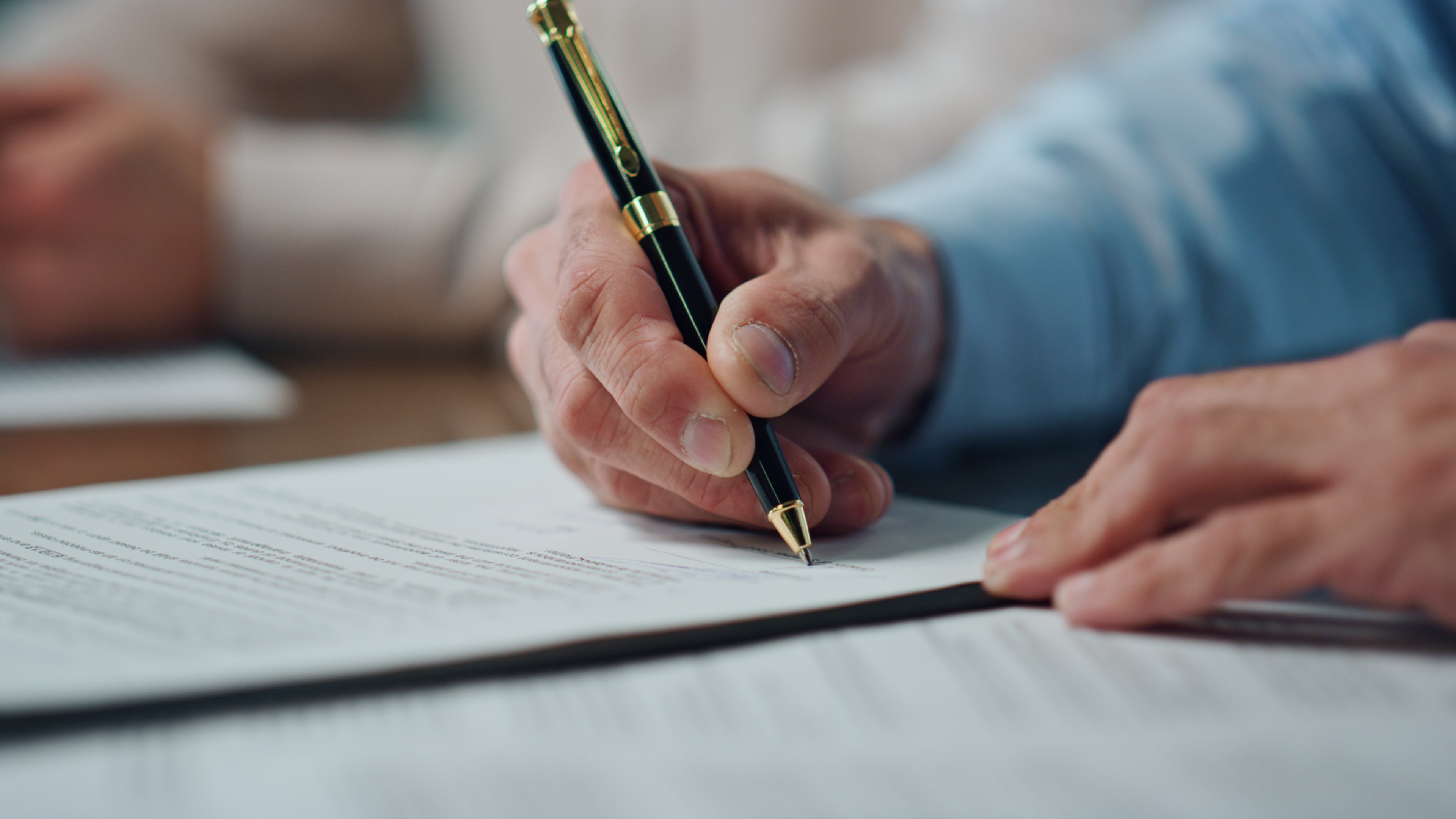 Person signing a document with a pen, close-up on hands and paper