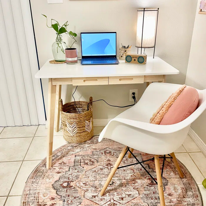 Reviewer&#x27;s photo of the desk in the color white, decorated with a plant, a desk lamp, a small speaker, and a laptop, with a white chair and pink pillow in front of it