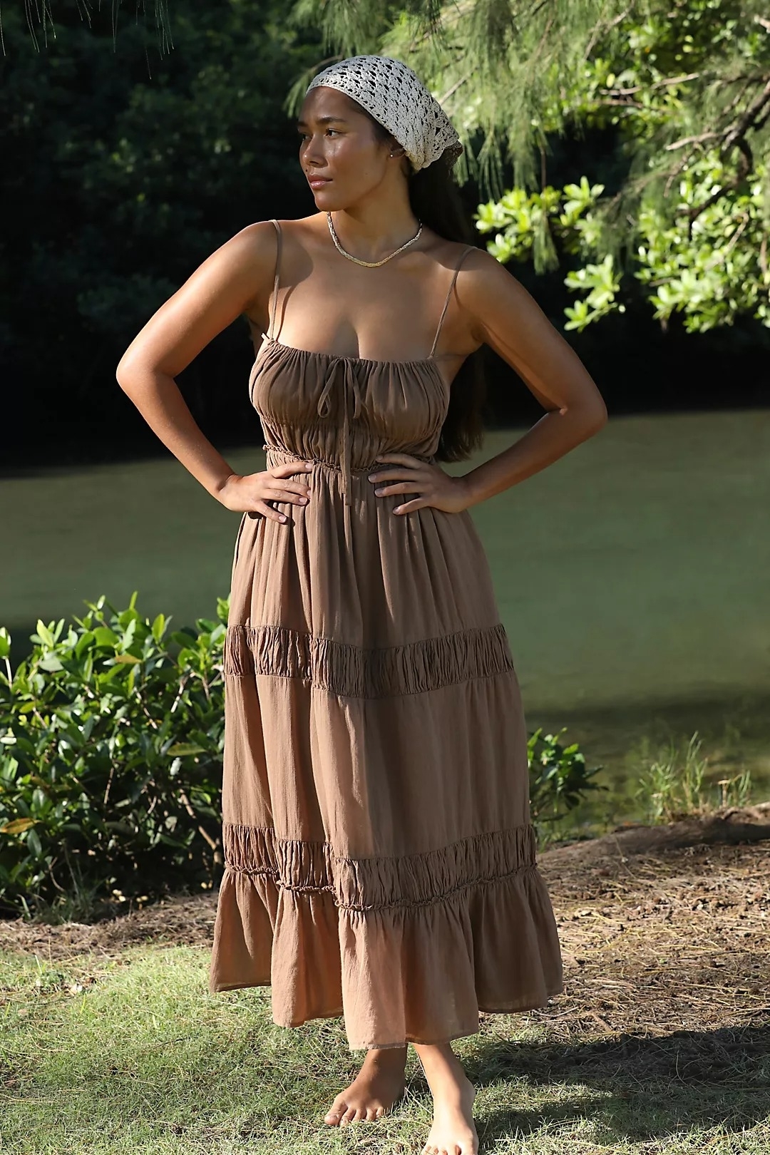 model in a tiered, sleeveless dress stands outdoors with hands on hips