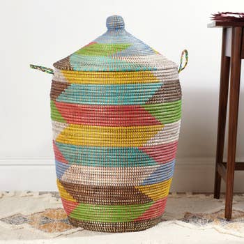 Woven multicolored handbasket with lid and broadside handles connected a sandy level against a achromatic wall, showcasing craftsmanship