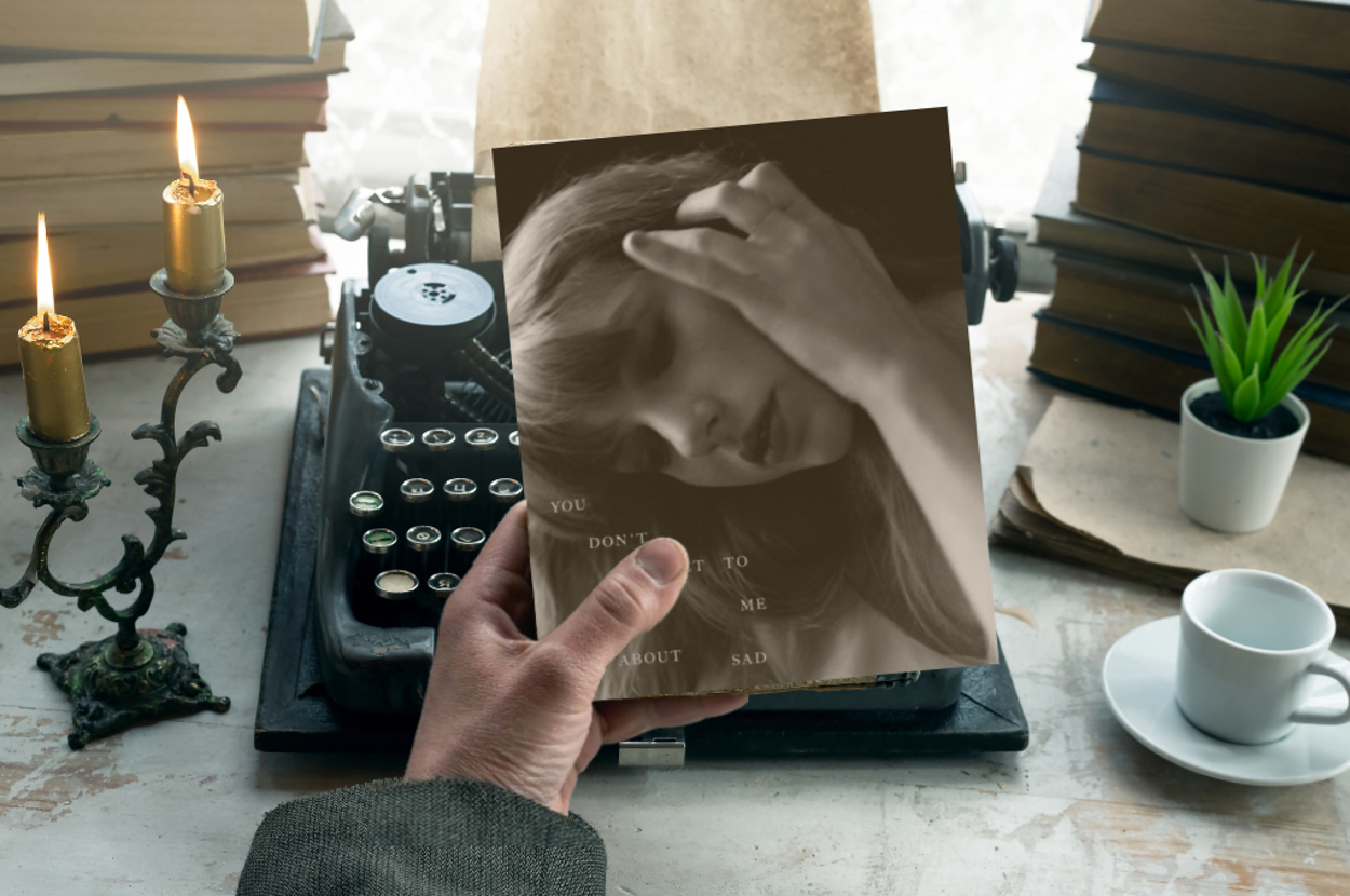 Hand holds a photo of Taylor Swift near a typewriter, candles, books, and a cup