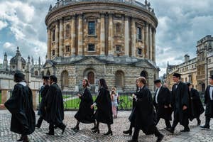 Graduates in black gowns walking by historical building