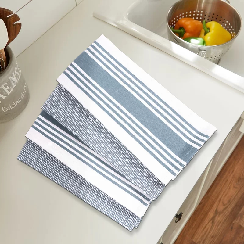 The dish towel set in the color blue folded on countertop with a bowl of vegetables in the background