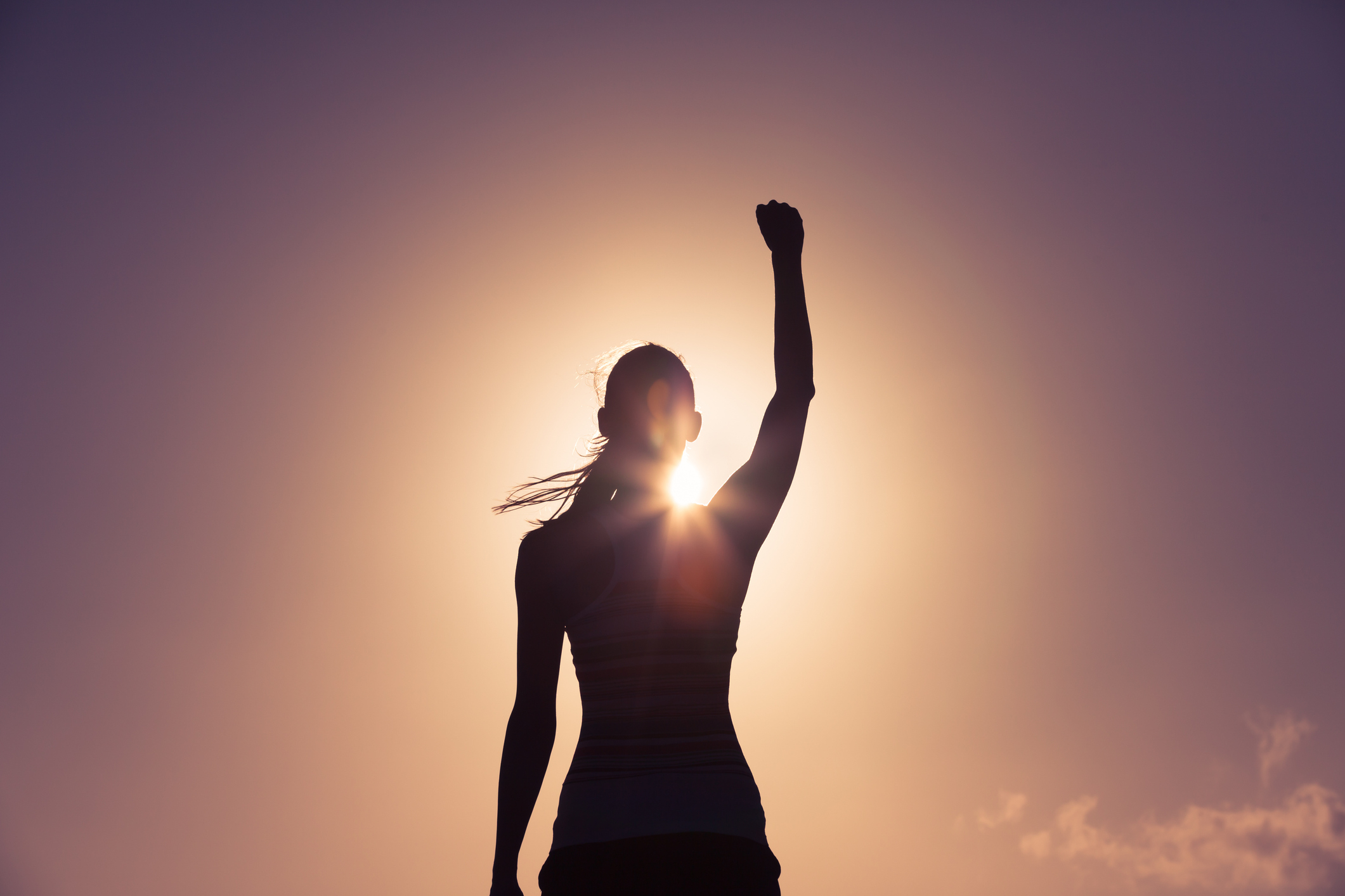 Silhouetted figure raising fist in the air against a bright backlight