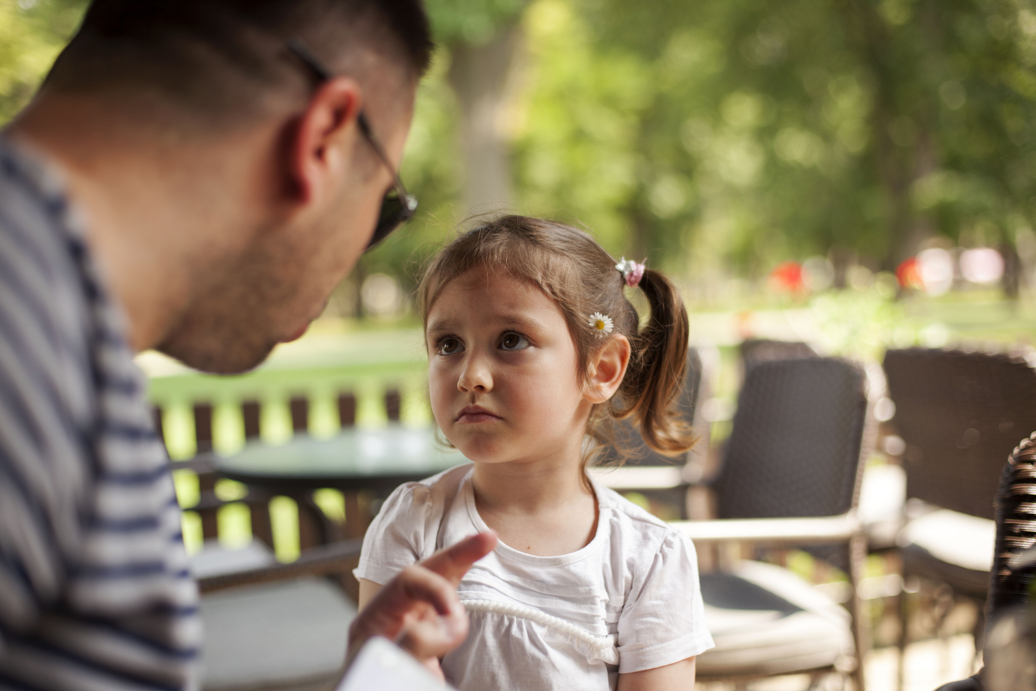 Adult talking to a focused young child outdoors, conveying a parent-child interaction