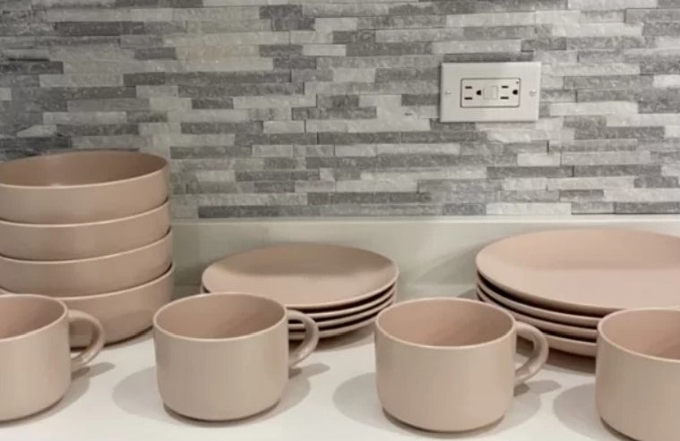 Reviewer&#x27;s photo of the set of stoneware dishes in the color blush pink, stacked and lined up on a kitchen counter