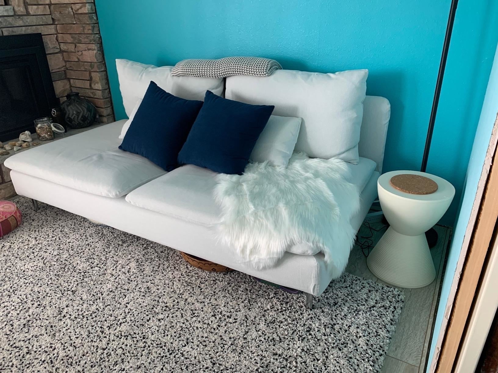 A modern   sofa  with pillows and a fur throw, adjacent  to a unsocial   broadside  table. Ideal for location  decor inspiration