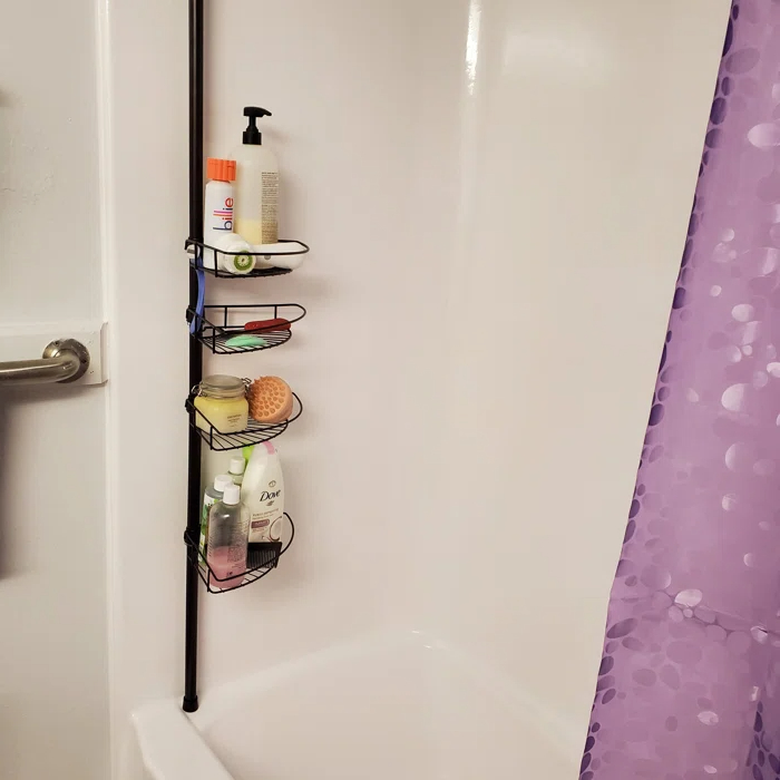 Reviewer&#x27;s photo of the tension pole shower organizer in the color bronze, holding various bath products next to a purple shower curtain