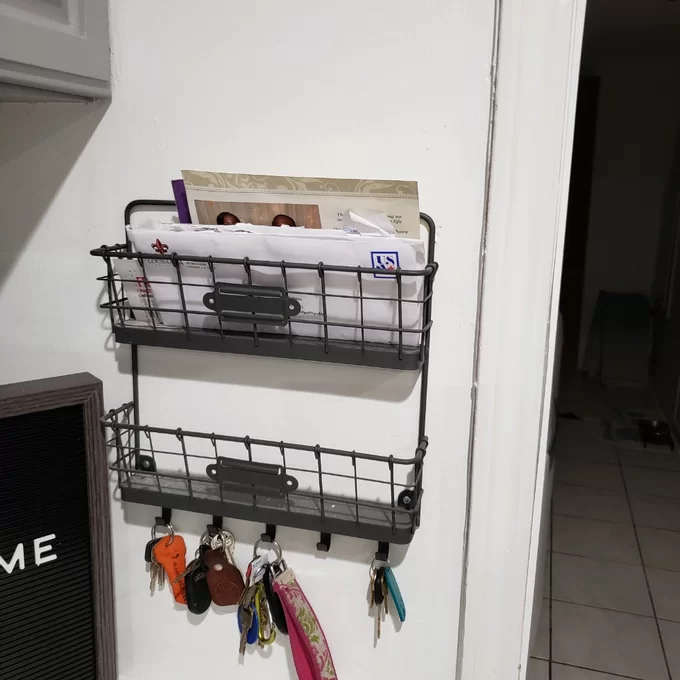 Reviewer&#x27;s photo of the wall organizer with mail in the top basket, an empty bottom basket, and four sets of keys hanging from five hooks