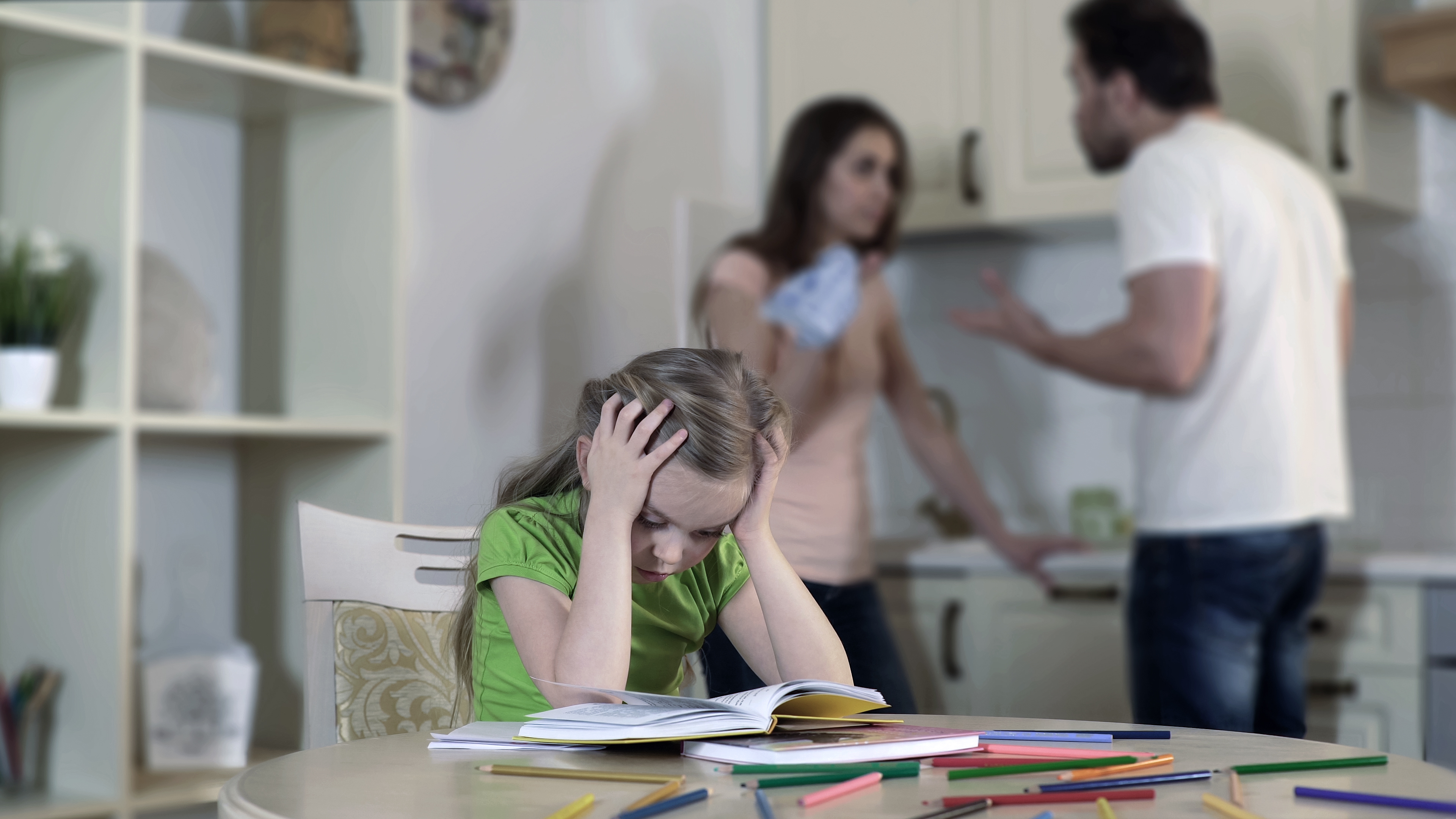 Child looks stressed studying while adults argue in the background, depicting family tension affecting children&#x27;s well-being