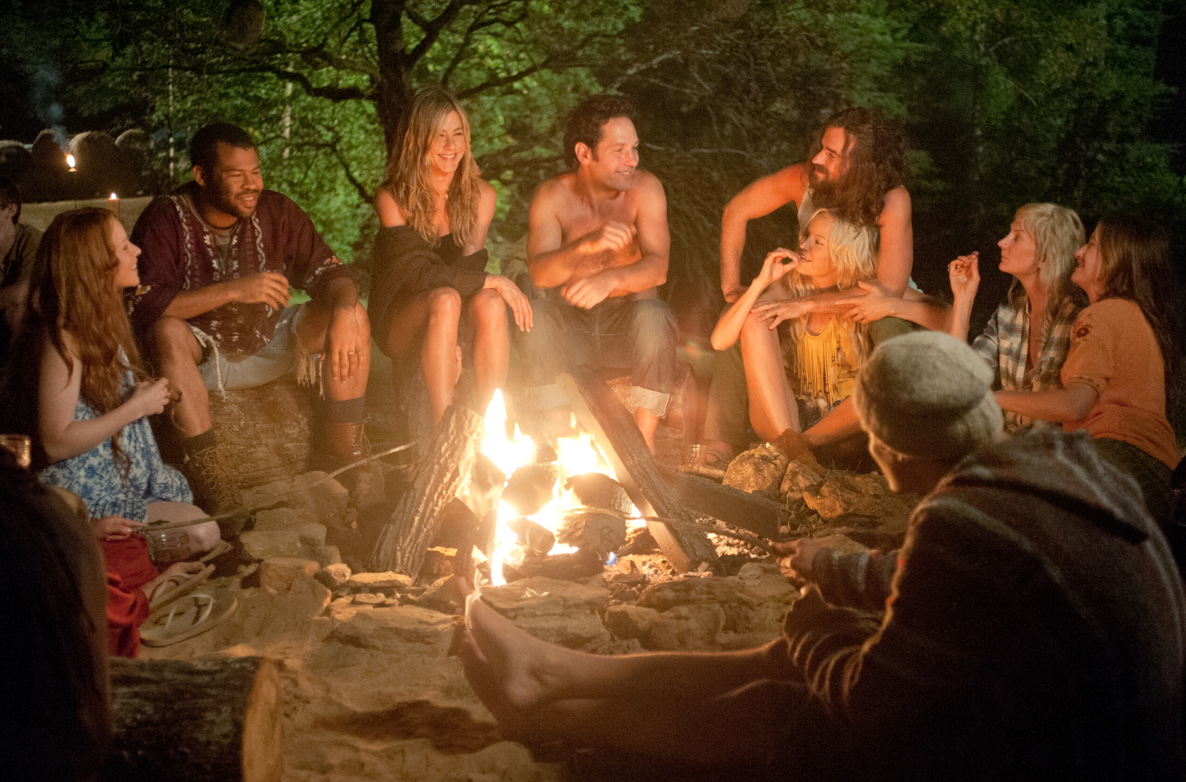 Group of people sitting around a campfire at night, engaged in conversation and laughter