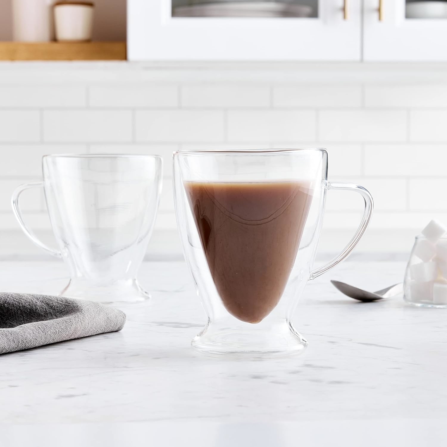 Double-walled glass mugs on a kitchen counter, one filled with coffee