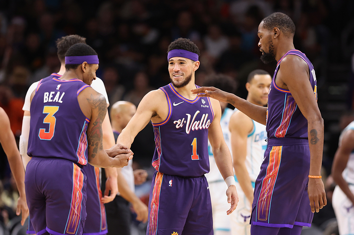 Phoenix Suns players on court in a huddle, exchanging fist bumps and gestures of teamwork