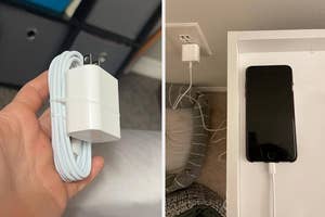 Hand holding a phone charger; another charger plugged into wall with phone charging on bedside