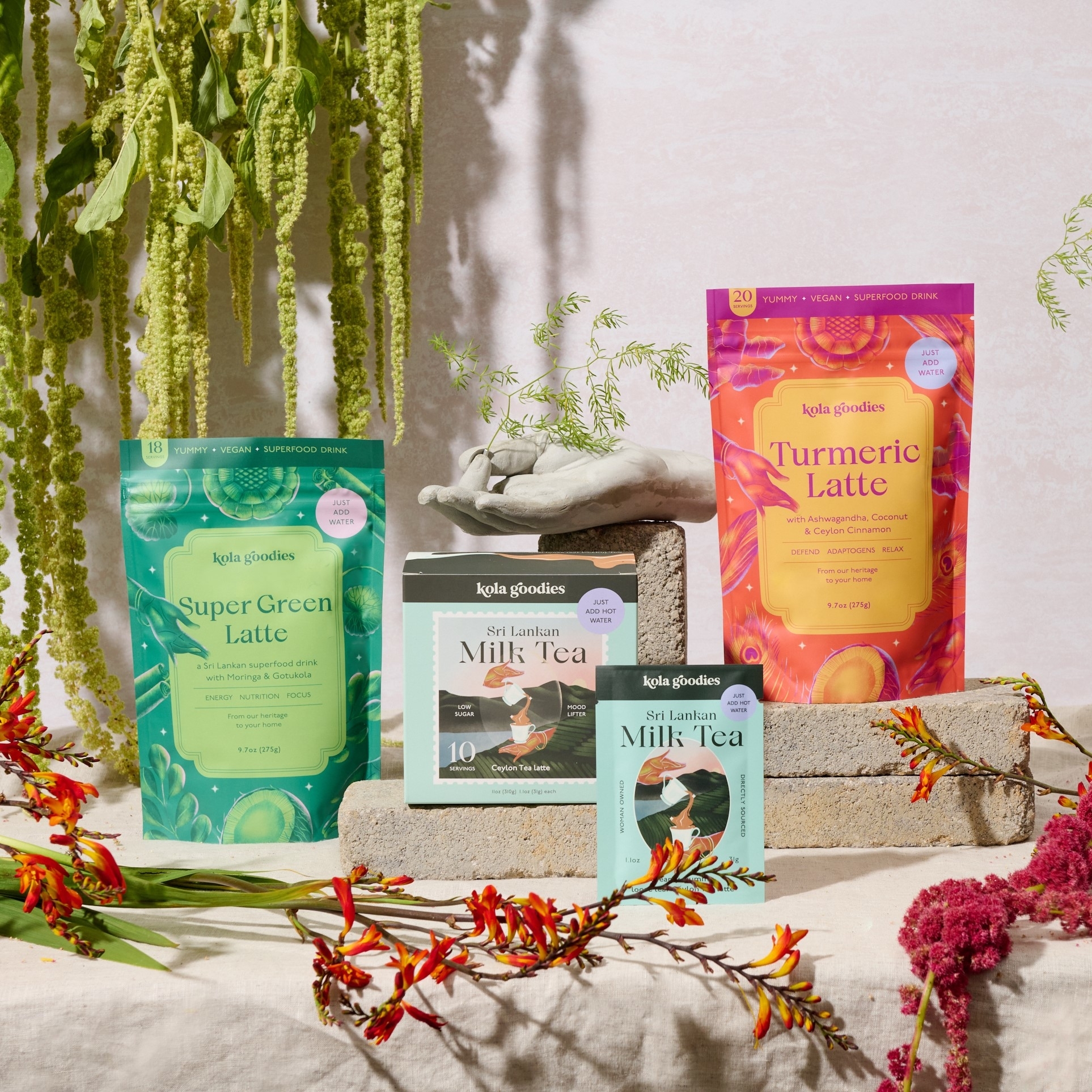 Assorted Kola Goodies beverage mixes displayed with decorative plants and stones