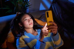 Woman lying on a couch looking at her smartphone screen, indoors, at night