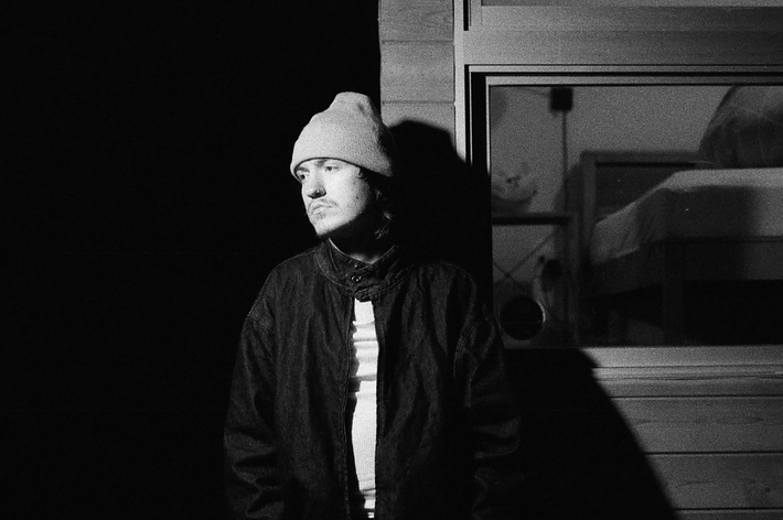 Man in beanie and jacket standing beside a building at night