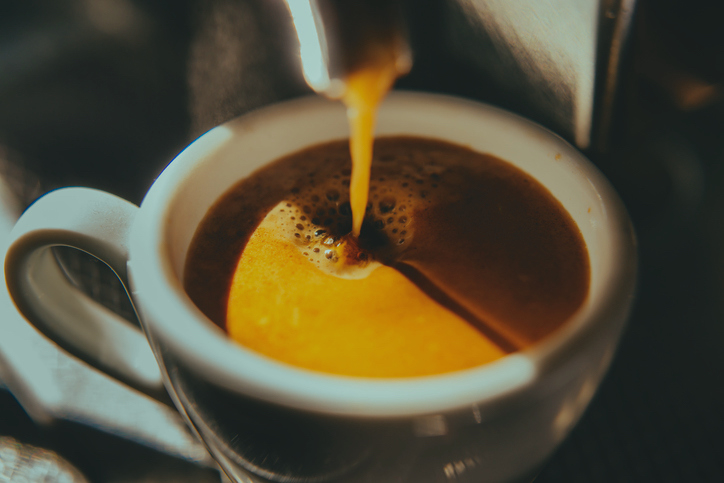 Coffee being poured into a white cup, close-up of the stream and bubbles forming on the surface