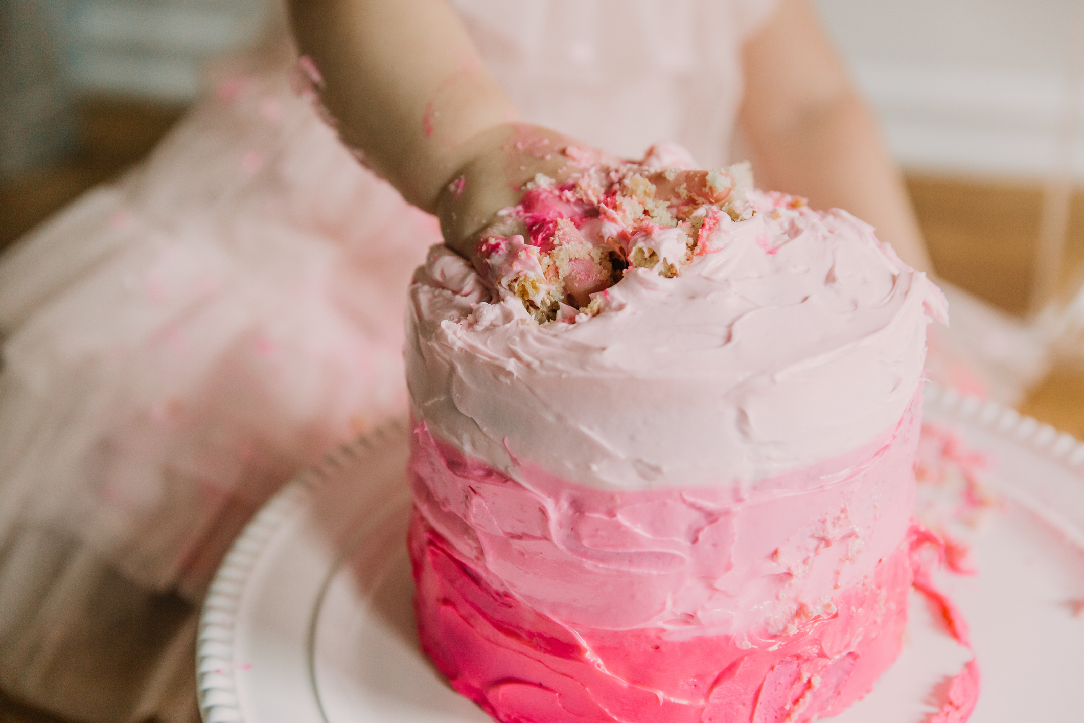 Child smashing hand into a pink frosted cake during a cake smash photo session