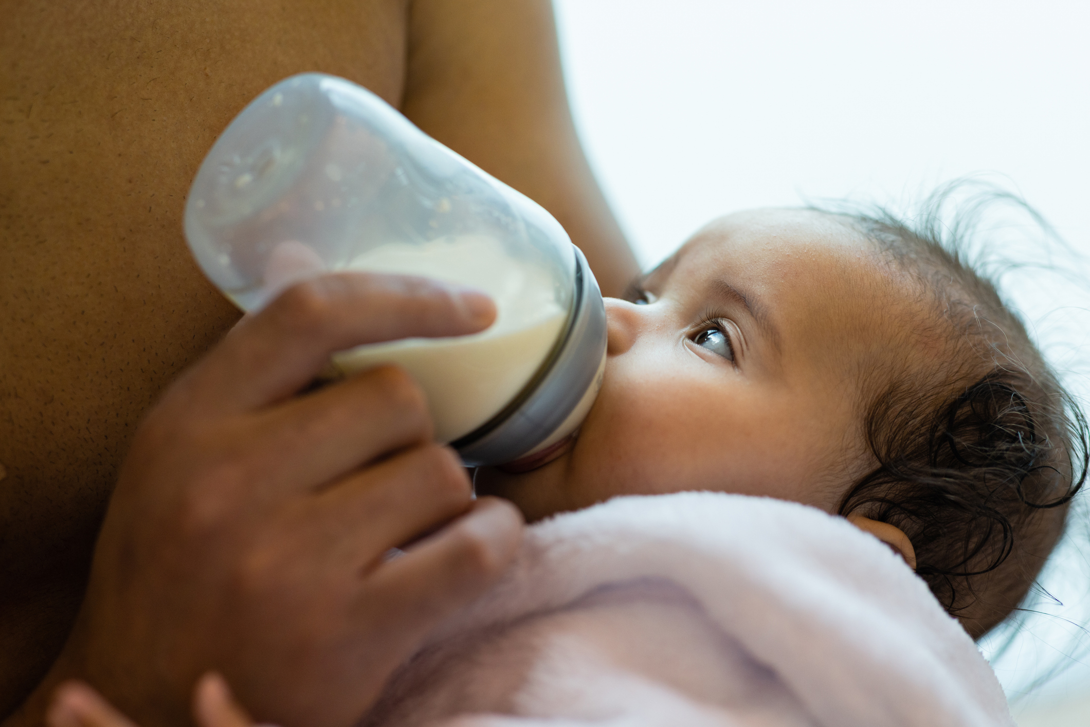 Infant being bottle-fed by a caregiver, close-up view, baby&#x27;s eyes gazing upward