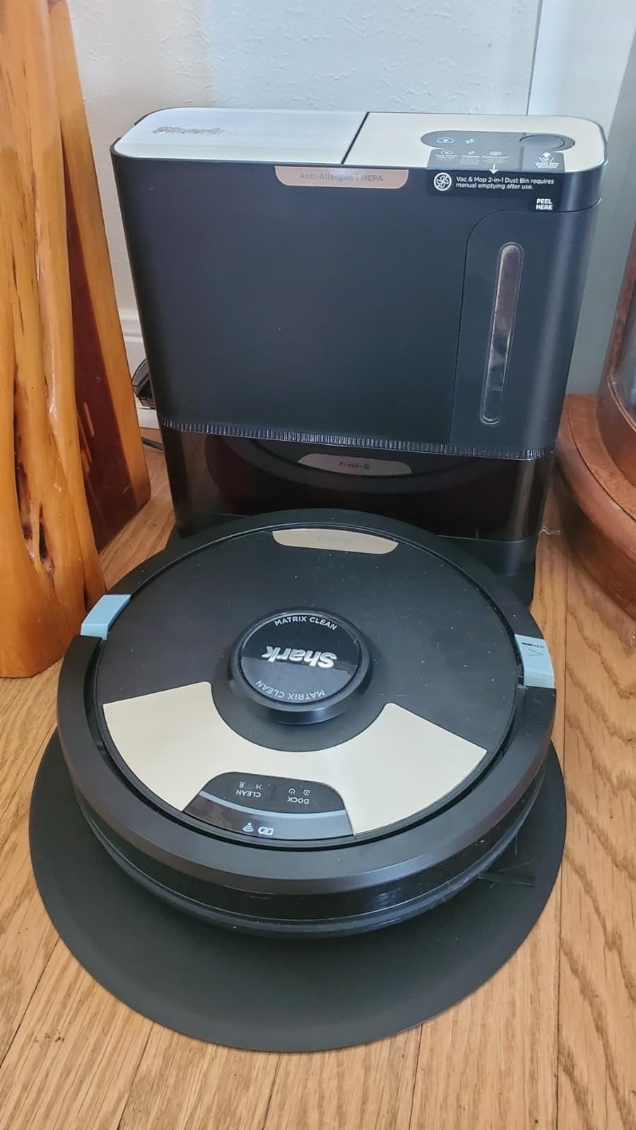 A robot vacuum cleaner is positioned in front of a stationary air conditioner unit in a home setting