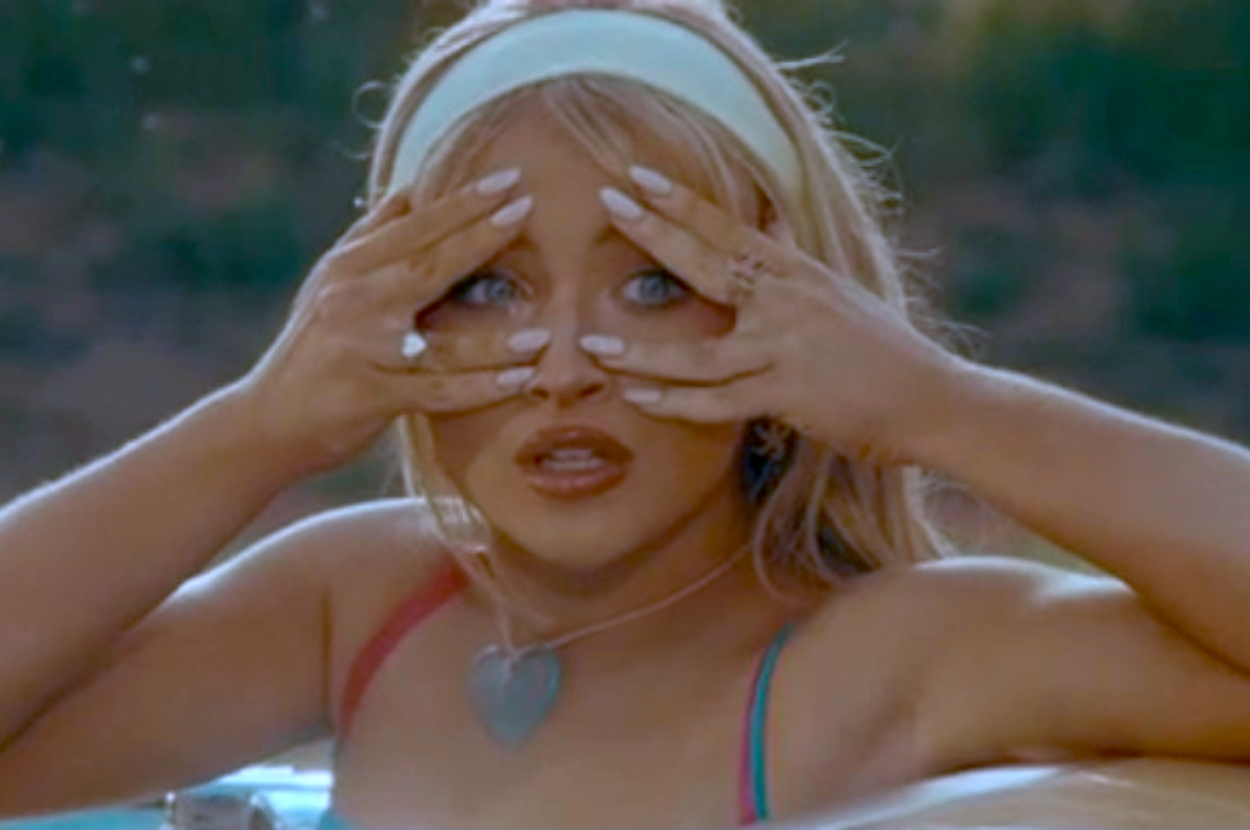 Person covering their eyes with hands, wearing a headband and heart-shaped necklace, in a playful pose