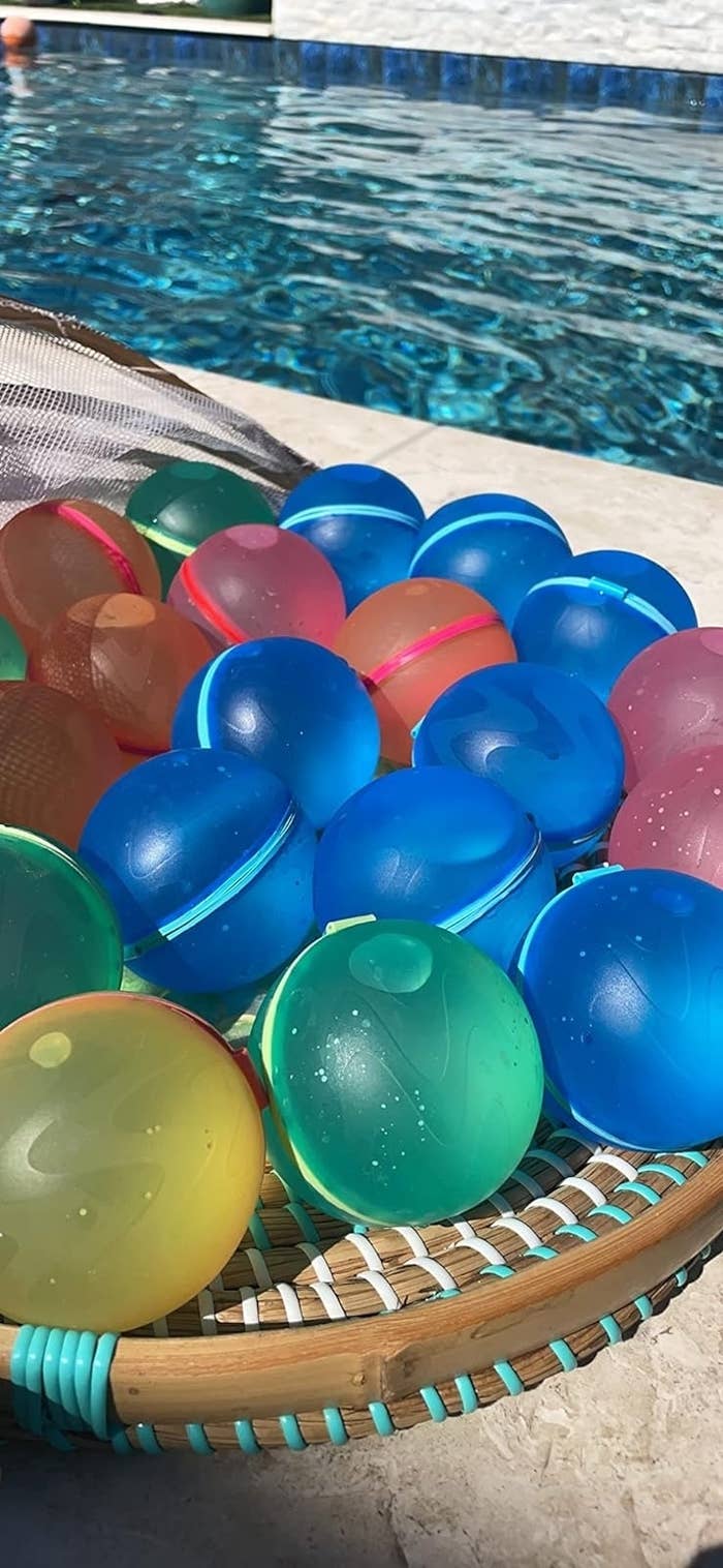 Basket of various colorful water balloons beside a pool, suggesting summer party accessories
