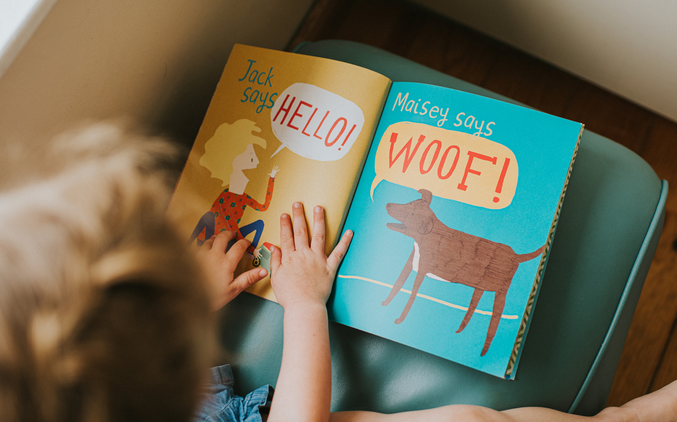 Child&#x27;s hands turning page in a book with &quot;HELLO!&quot; and &quot;WOOF!&quot; text