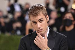 Justin Bieber in a black suit and gold watch posing with a hand on chin