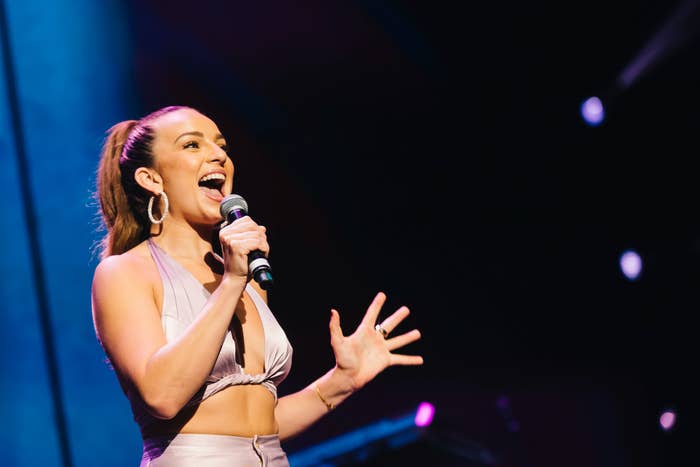 Woman performing on stage with a microphone, wearing a stylish crop top and high-waisted pants