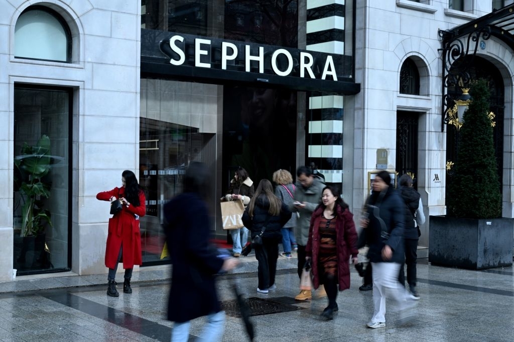Individuals walk by a Sephora store; motion blur conveys their brisk pace