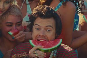 Harry Styles smiles, holding a watermelon slice, surrounded by blurry faces