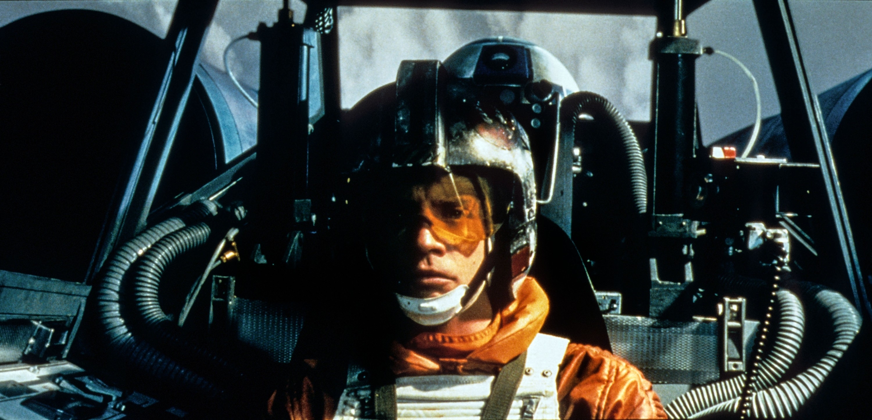 Luke Skywalker in pilot gear sitting in the cockpit of an X-wing fighter