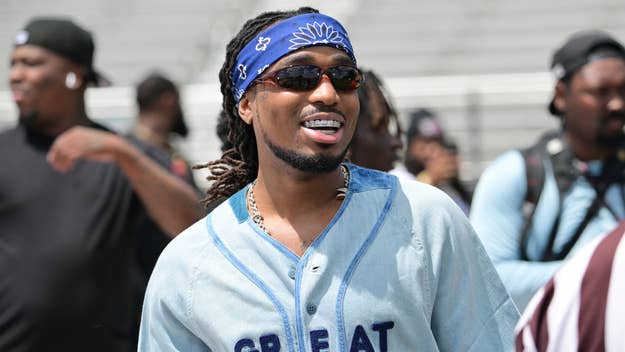Person smiling, wearing a bandana, sunglasses, and a jersey with the word "GREAT" across it, amidst a crowd