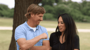 Chip and Joanna Gaines from Fixer Upper sitting under a tree, one playfully elbowing the other while conversing