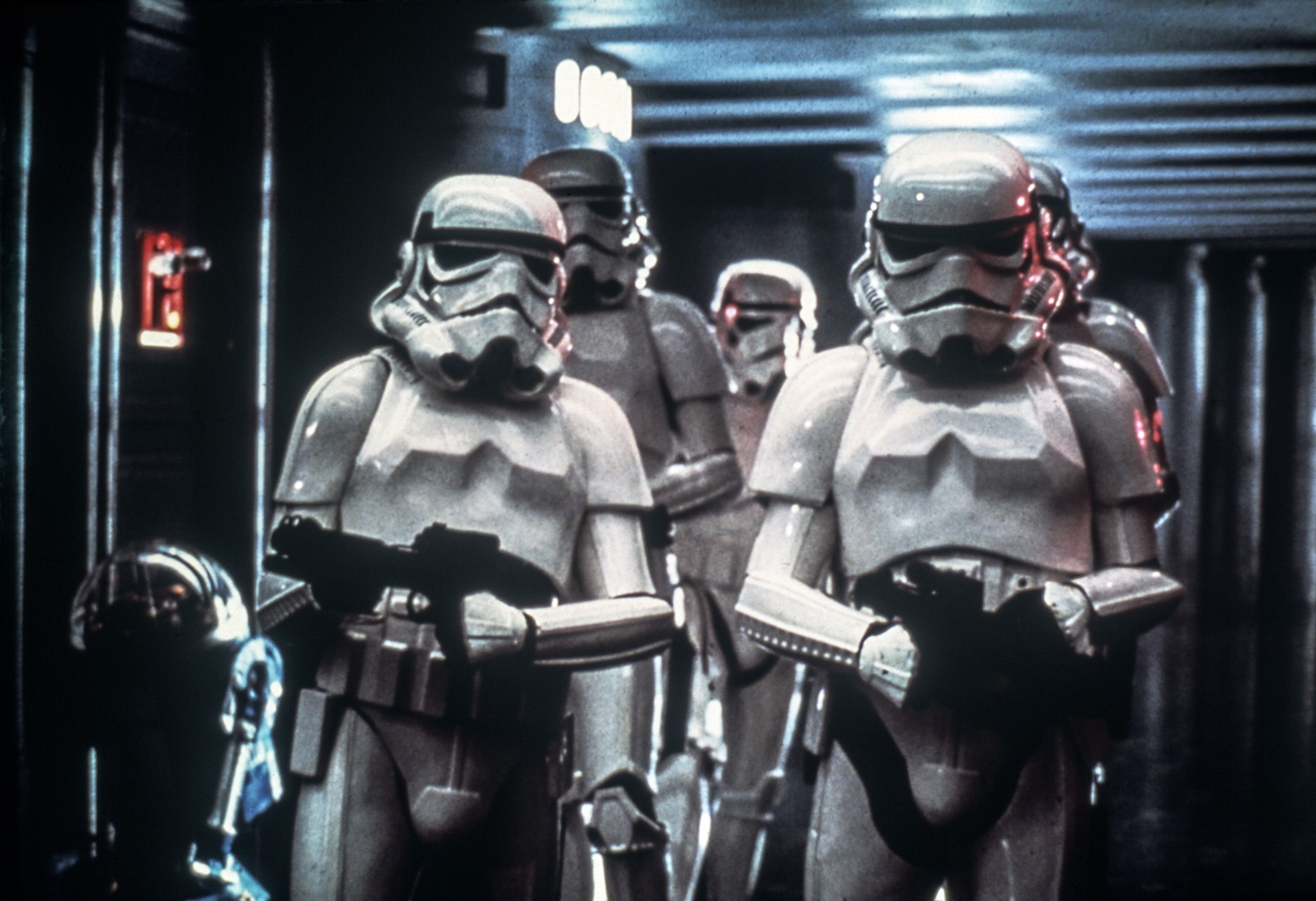 Group of Stormtroopers from Star Wars with blasters, alongside a black astromech droid in a spaceship corridor