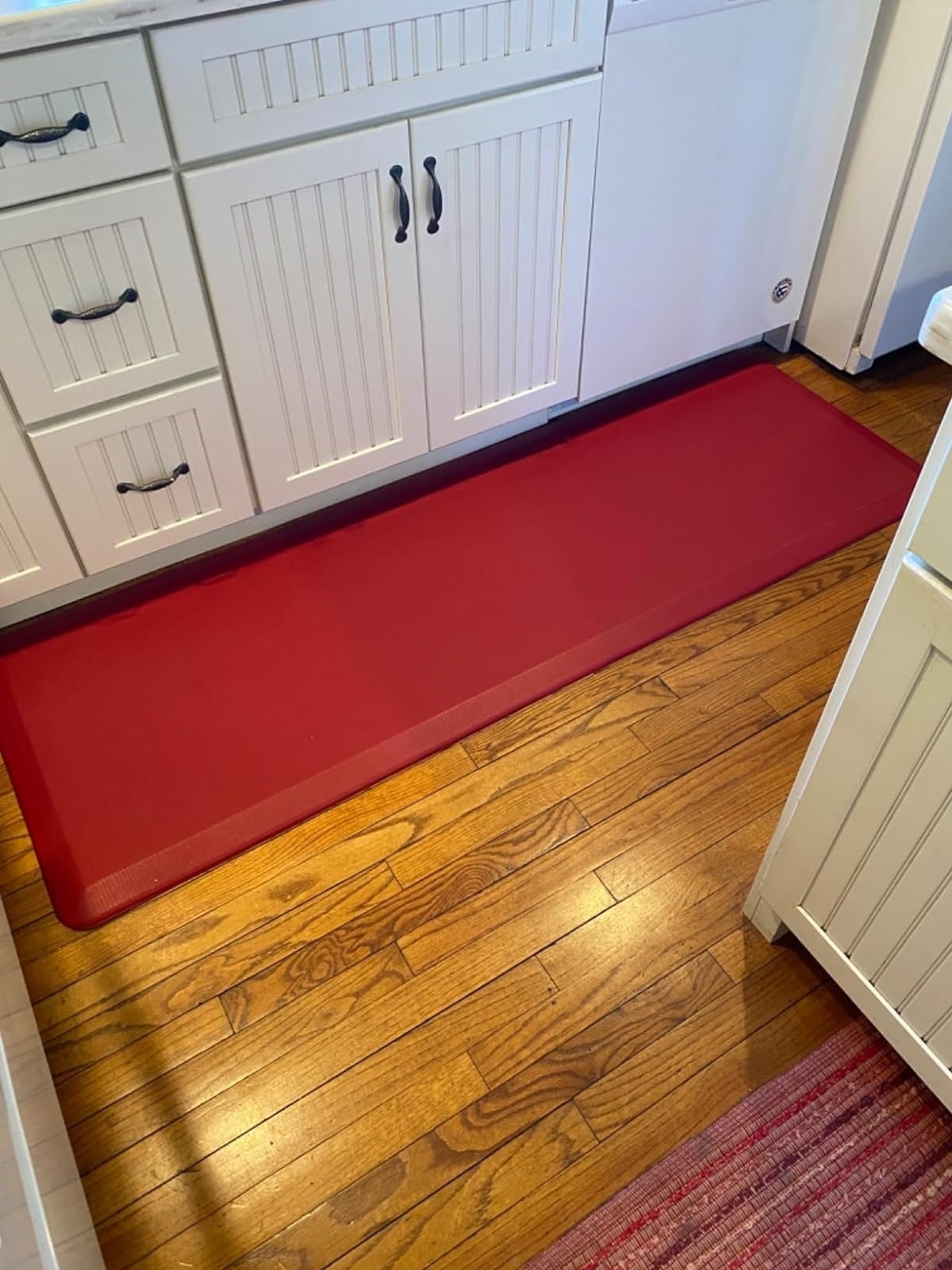 Red anti-fatigue kitchen mat in front of a white cabinet, suitable for long-standing comfort while shopping for kitchenware