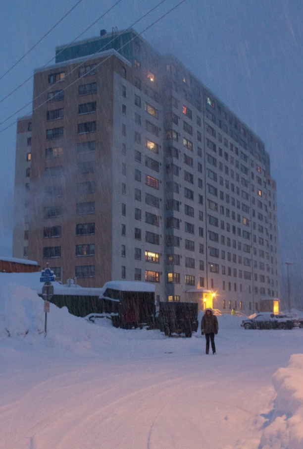 Person standing in front of a multi-story building in heavy snowfall at dusk