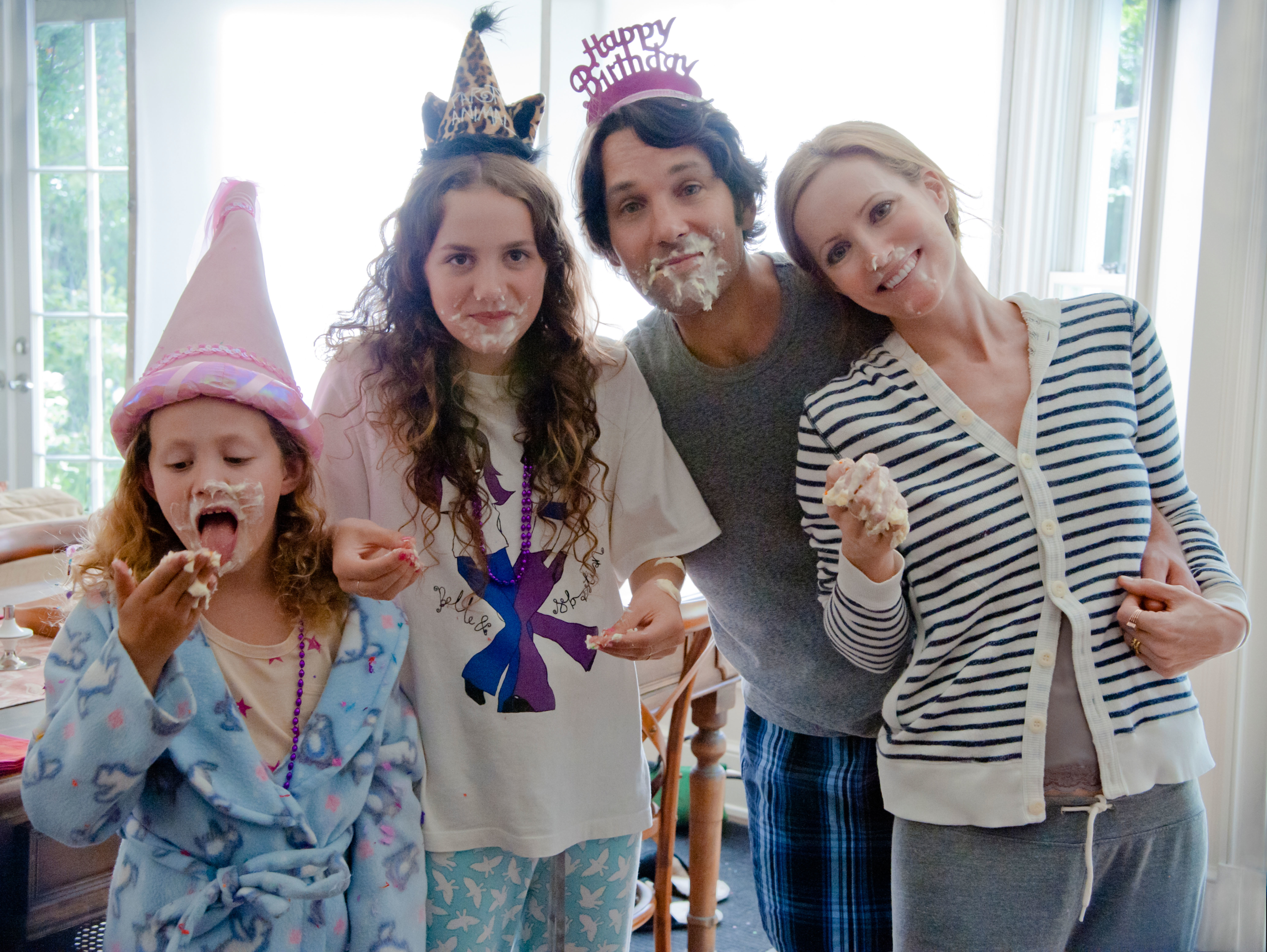 Family celebrating a birthday with cake; two children and two adults, smiling, with party hats