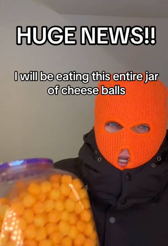 Person in black attire and orange mask holding a jar of cheese balls, text &quot;HUGE NEWS!! I will be eating this entire jar of cheese balls&quot; above
