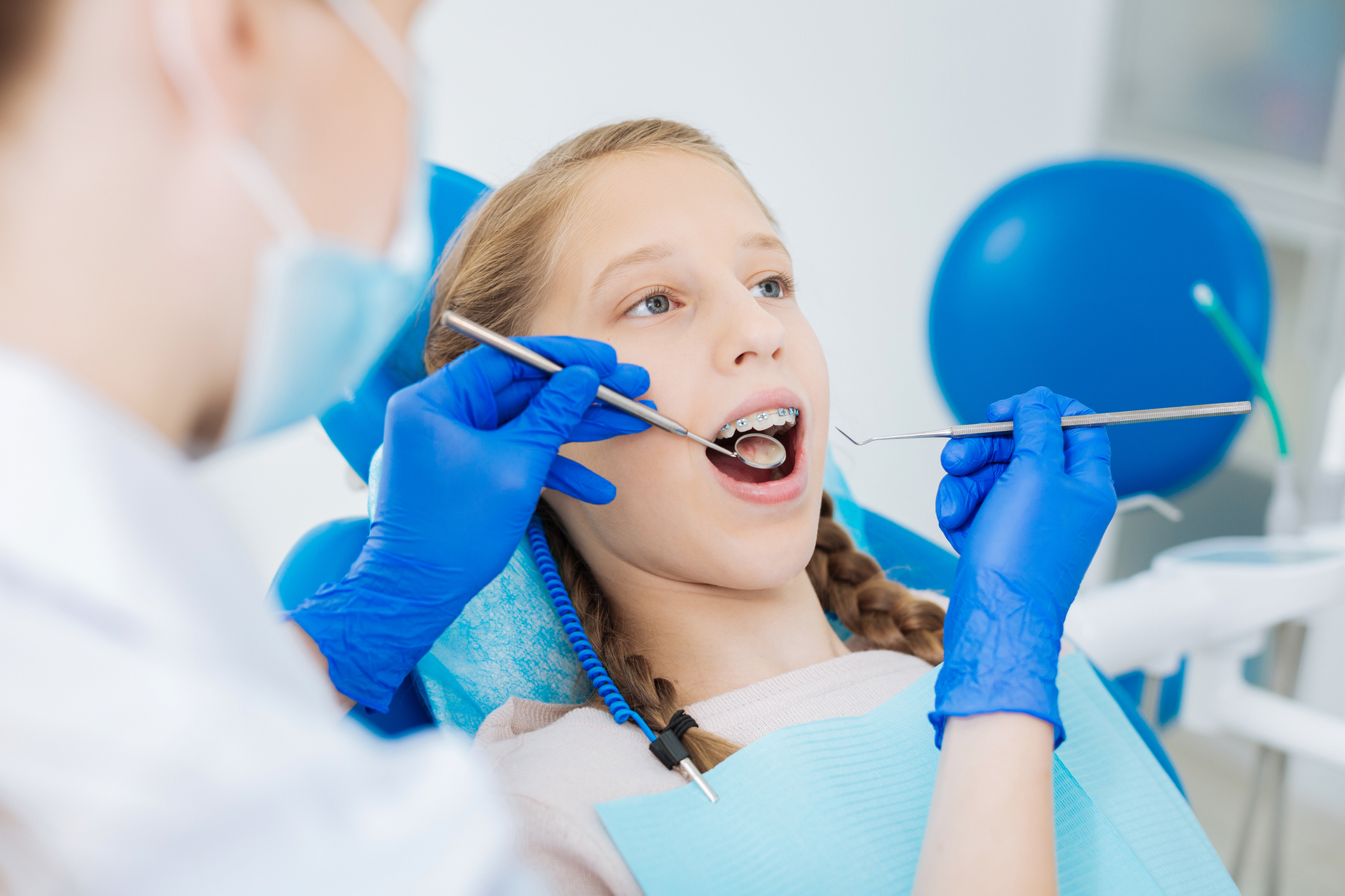 Young girl having a dental checkup with a dentist using tools. She looks calm. The setting suggests routine oral care