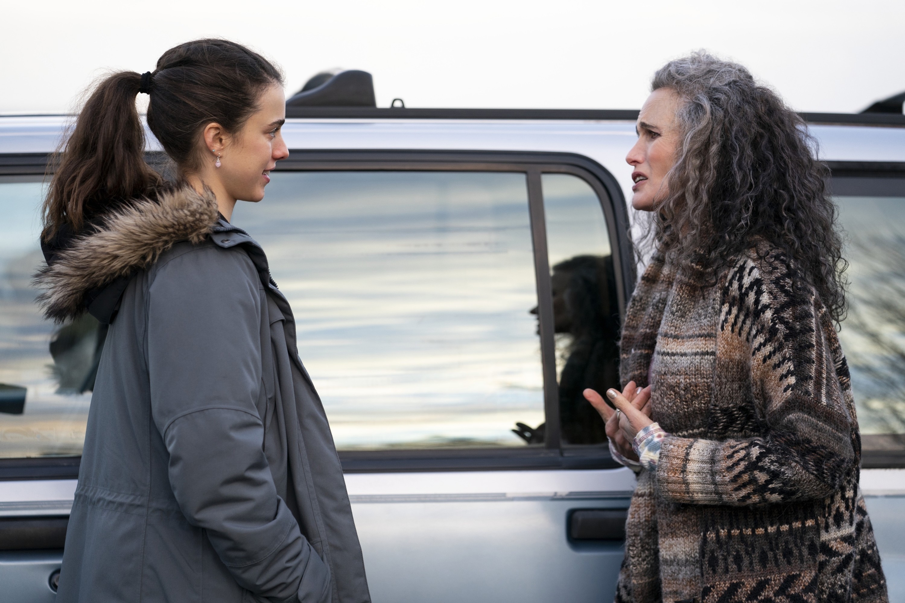 Two actresses on set talking beside a vehicle, dressed in character for a scene