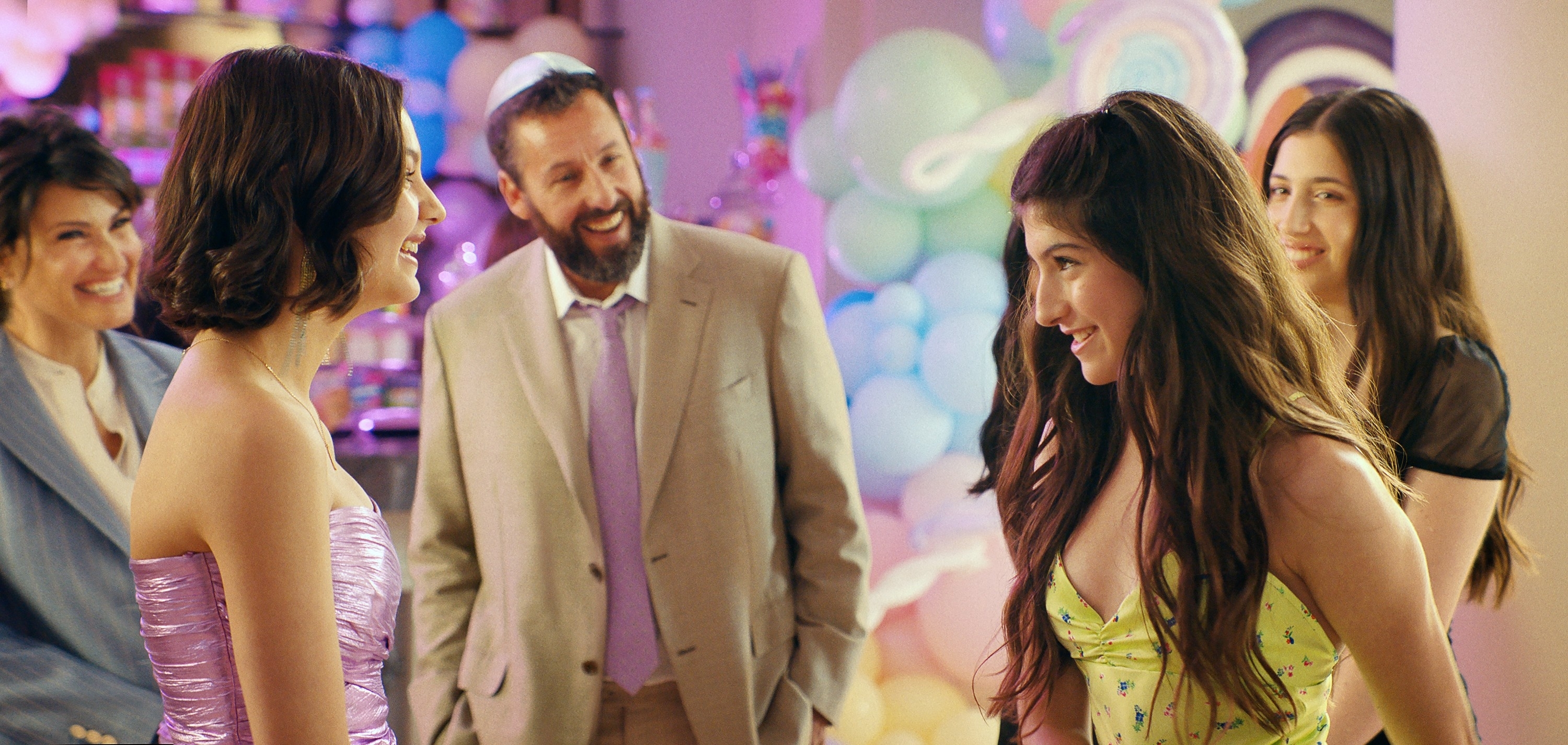 Group of people smiling at a social event, one in a strapless pink dress, another in yellow floral