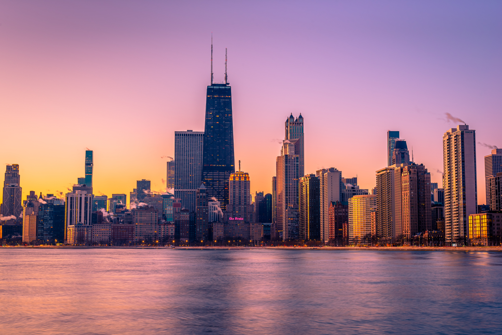 Chicago skyline at sunset with reflections on the water.
