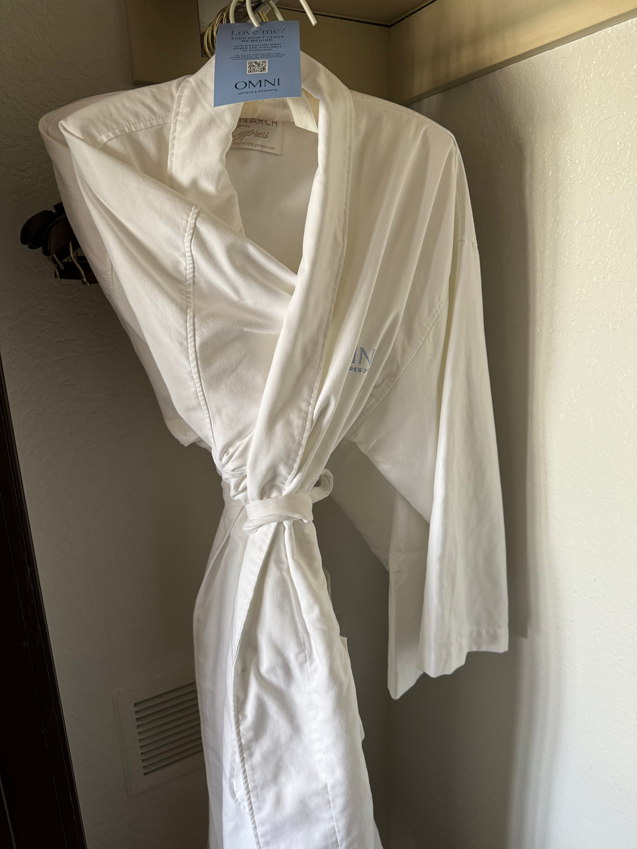 White bathrobe with &quot;Omni&quot; brand logo hanging on a door, possibly from a hotel room